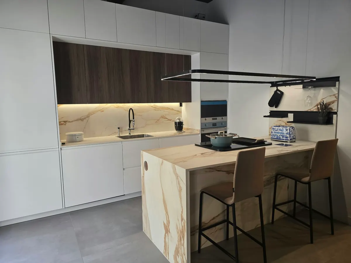 Cocina blanca con altos de nogal e isla de efecto mármol con taburetes